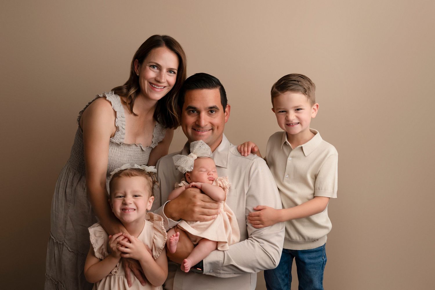 Family embraces and smiles together during indoor portrait session with warm neutral tones.