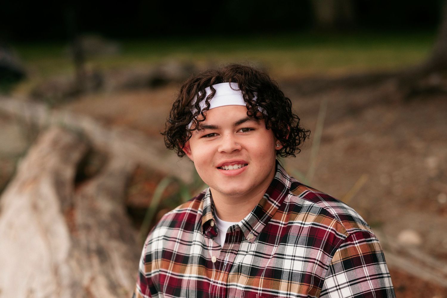 A person wearing a plaid flannel shirt sits outdoors on a sunny day among natural rocks and foliage.