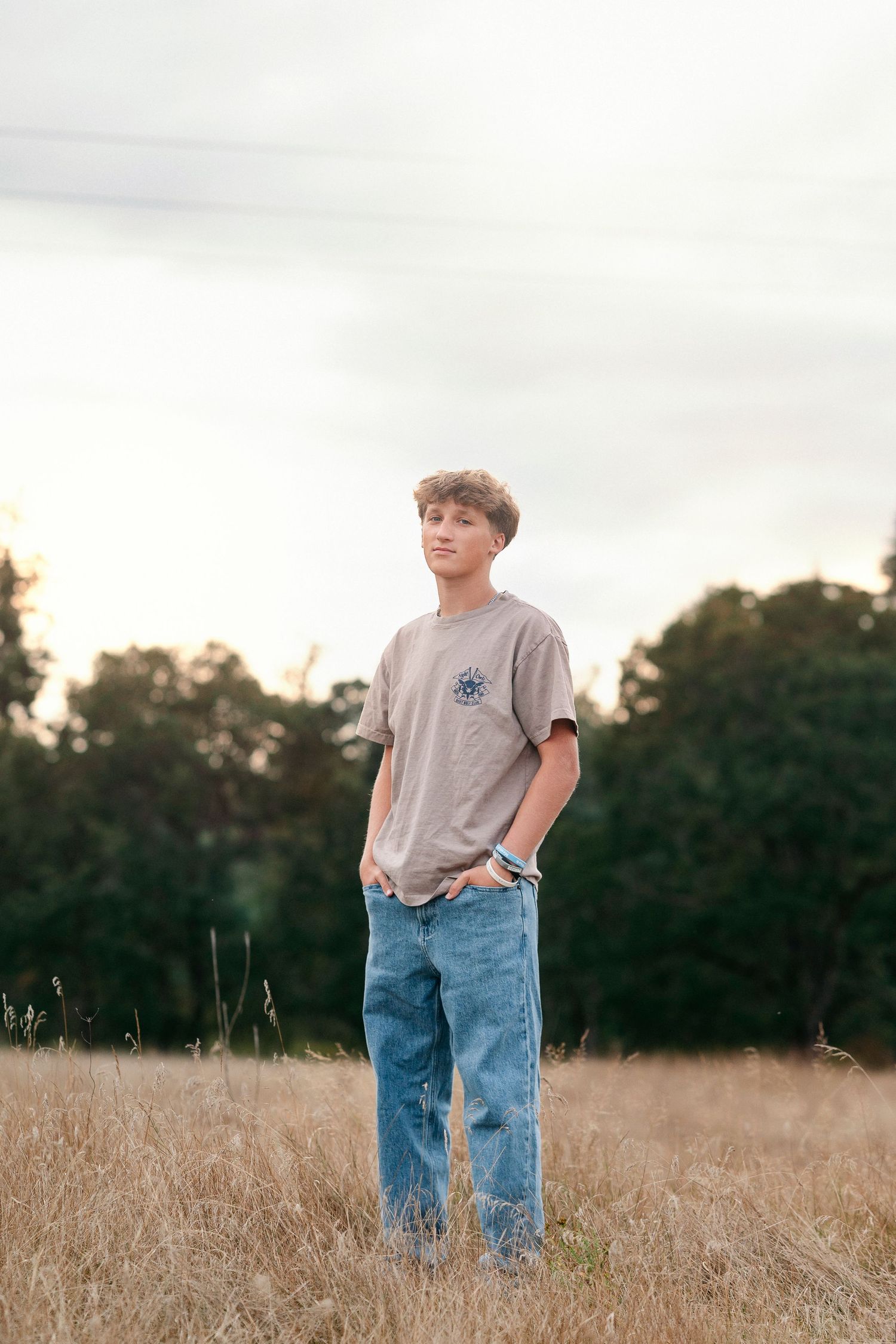 Person in a gray t-shirt and jeans stands thoughtfully in a golden wheat field at sunset.