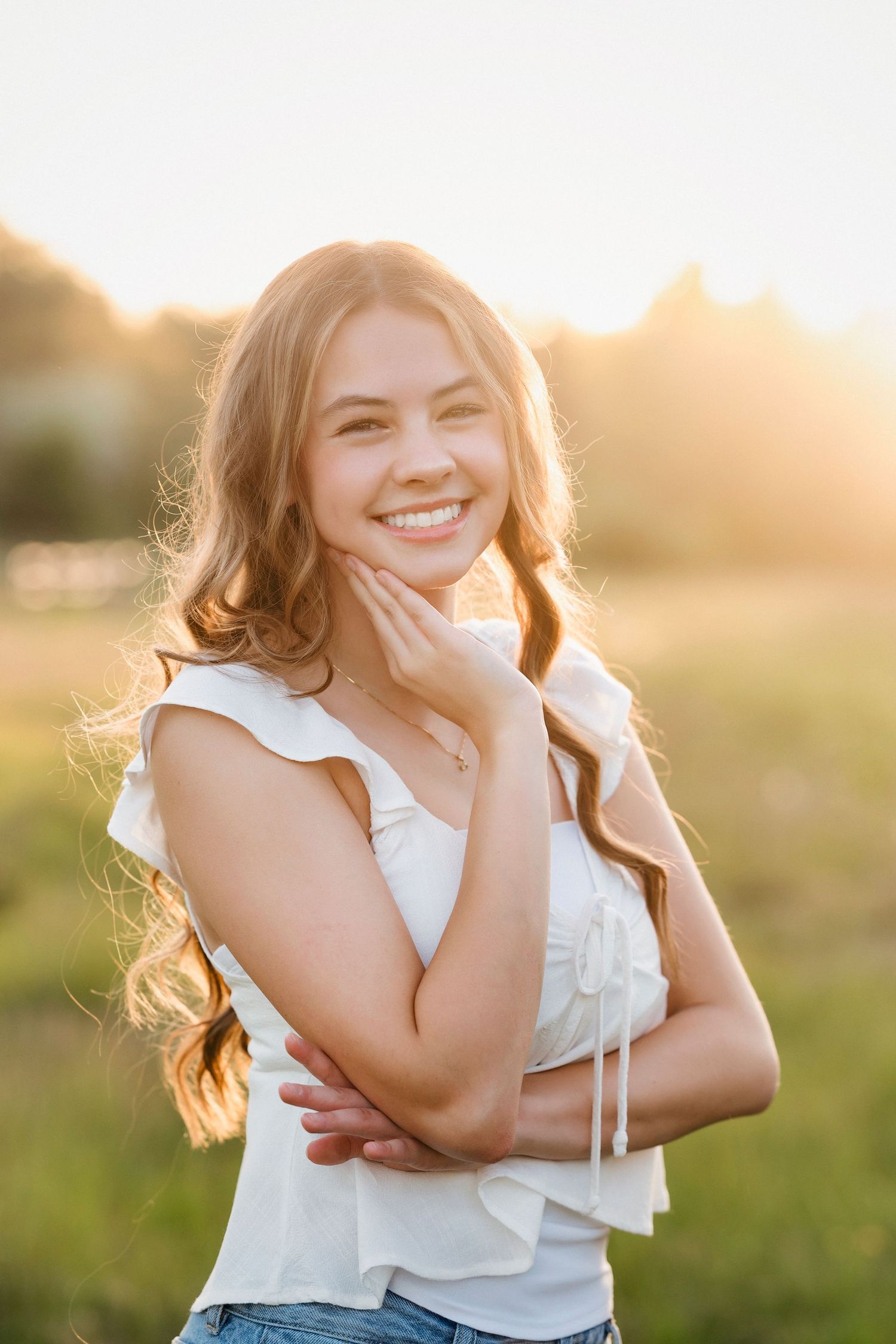 Portrait of someone in a white ruffled top smiling outdoors during golden hour sunset in a grassy field.