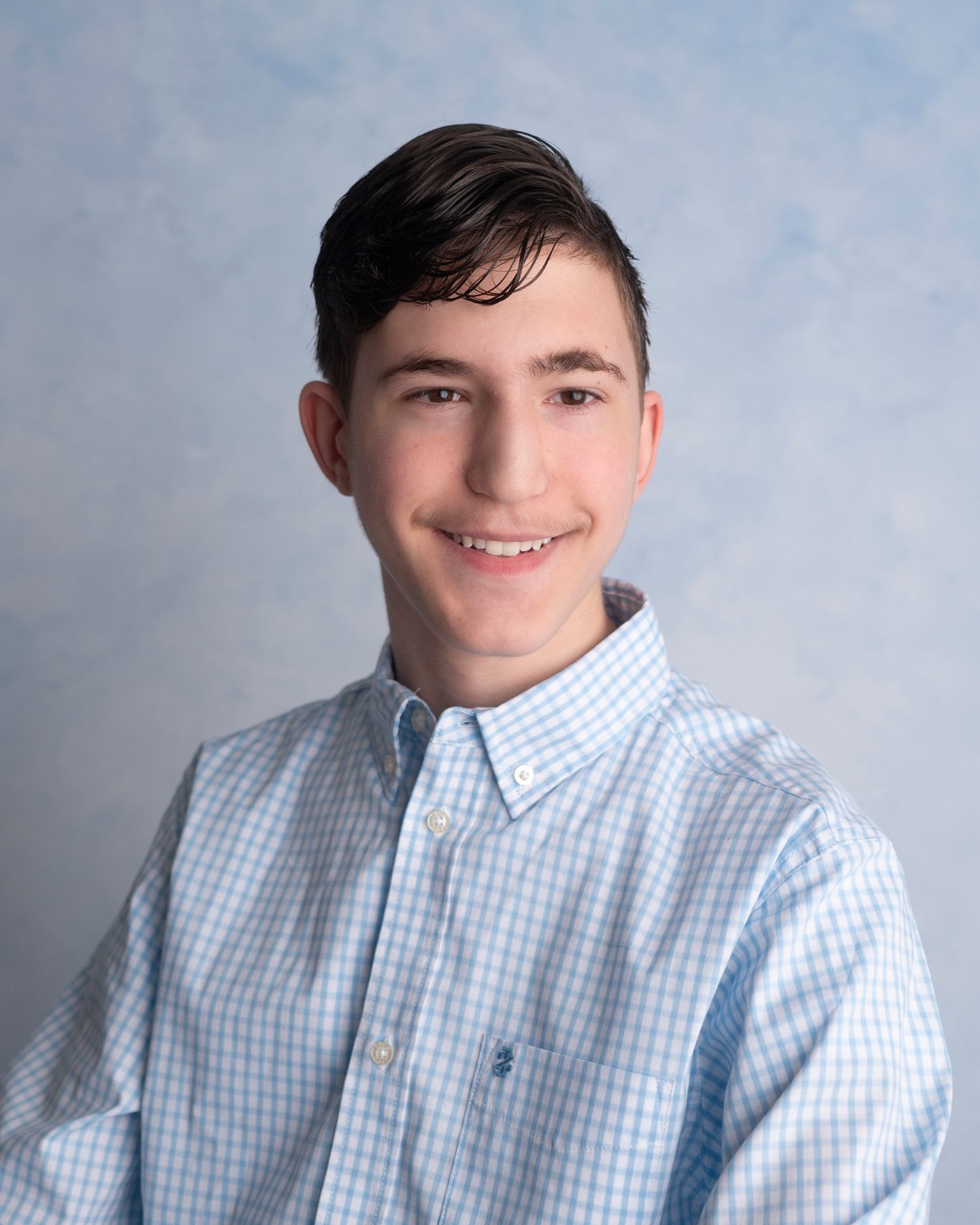 Blue checkered button-up shirt against grey studio backdrop in professional headshot lighting.