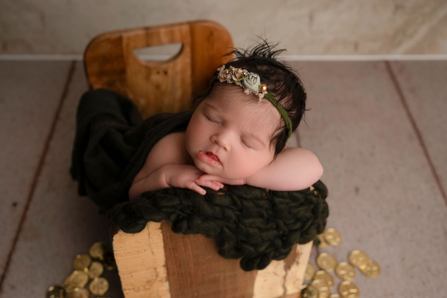 Sleeping newborn in black wrap posed in wooden bowl with gold decorative elements.