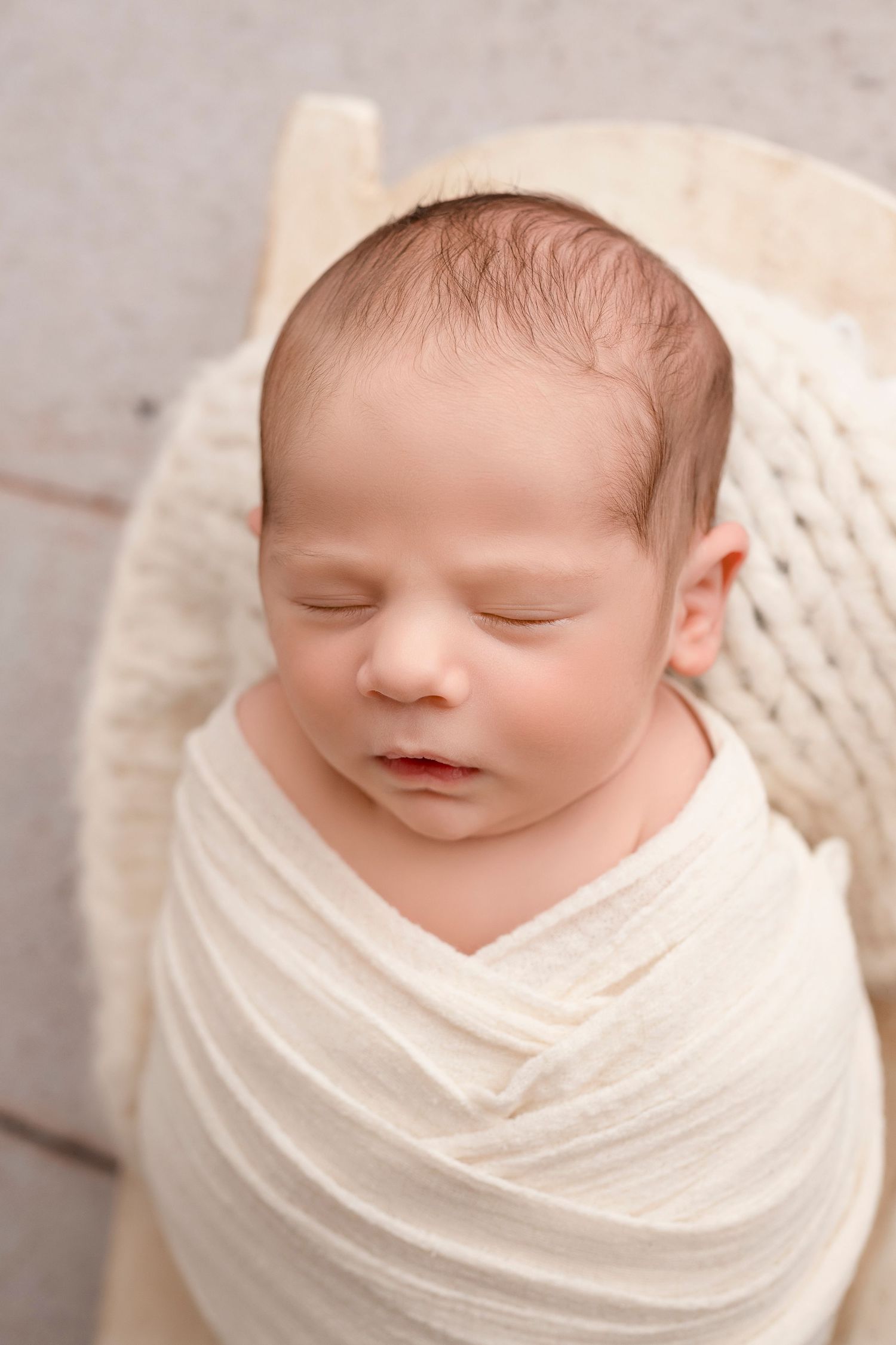 Sleeping newborn baby wrapped in soft white swaddle blanket shown in series of peaceful close-up portraits.
