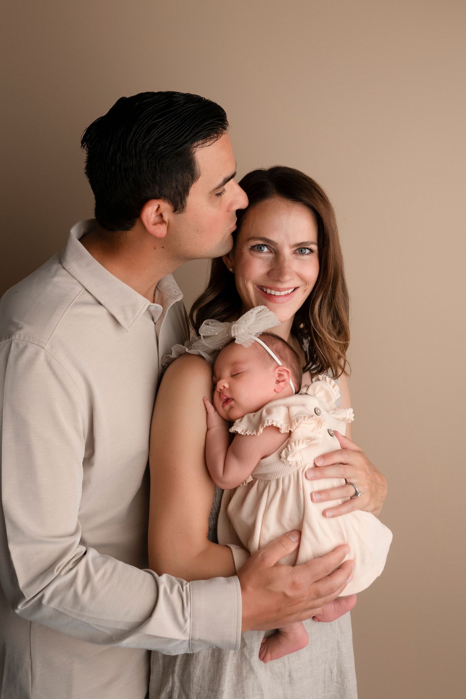 A heartwarming family photo sequence capturing intimate moments between parents and their infant against a beige backdrop.