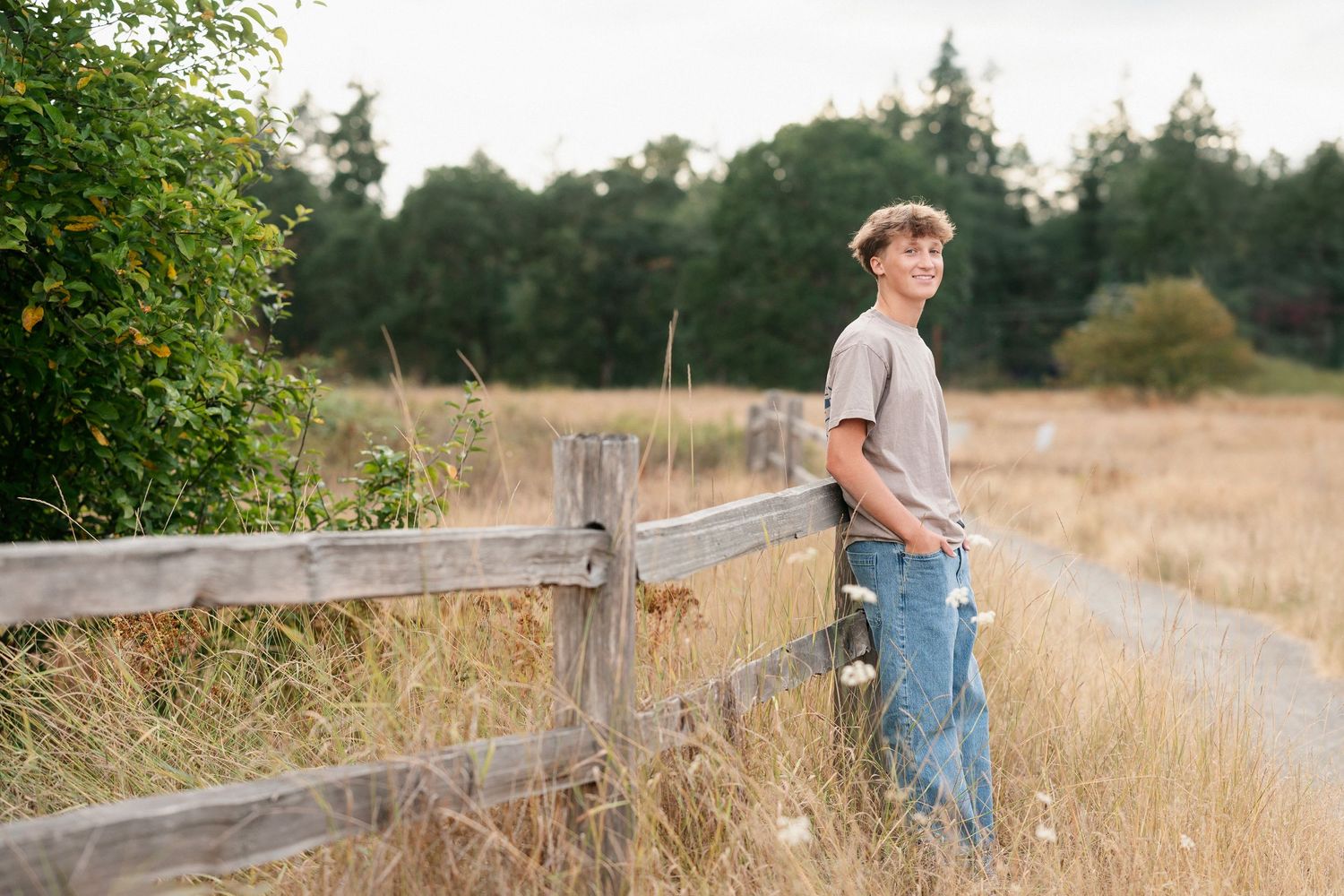A rustic wooden fence stretches along a dry grass field on a sunny summer day.