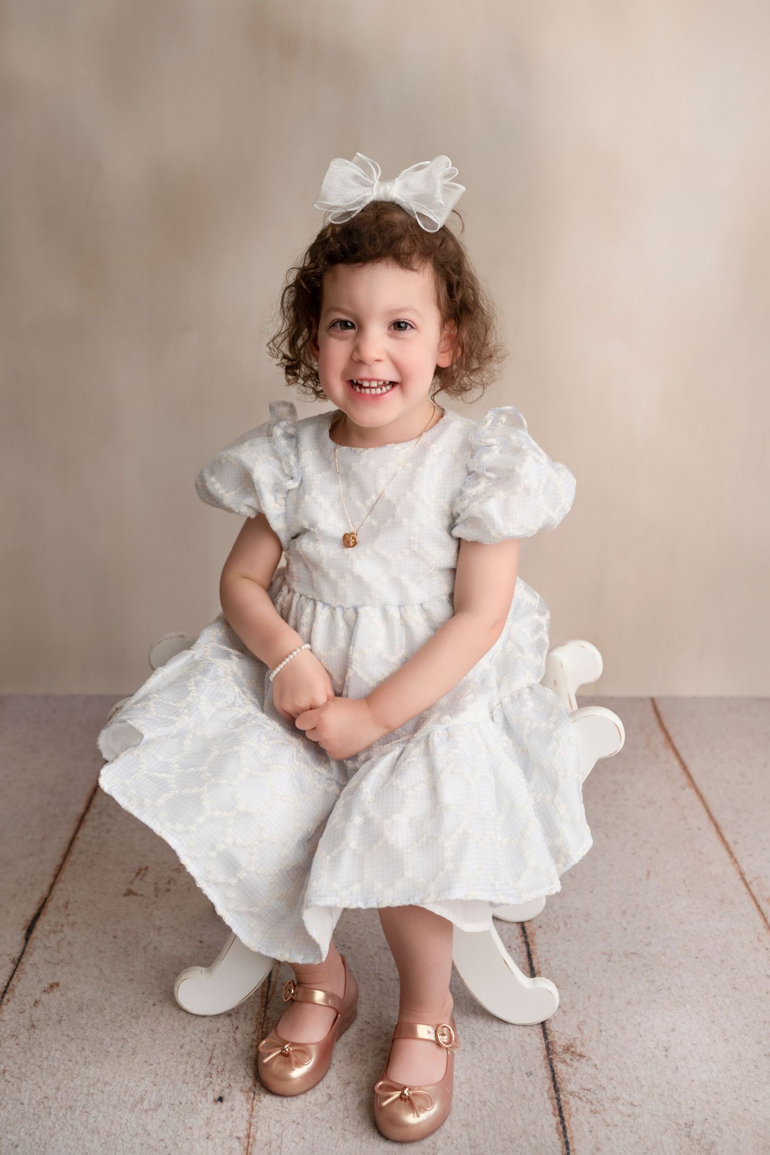 A series of photos showing a small child in a white lace dress and gold shoes sitting on a neutral backdrop.
