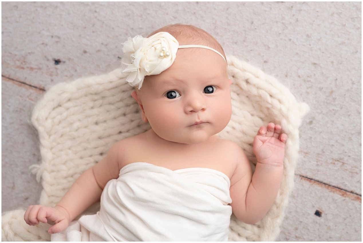 A baby wearing a white wrap lies on a soft textured blanket in a natural light setting.