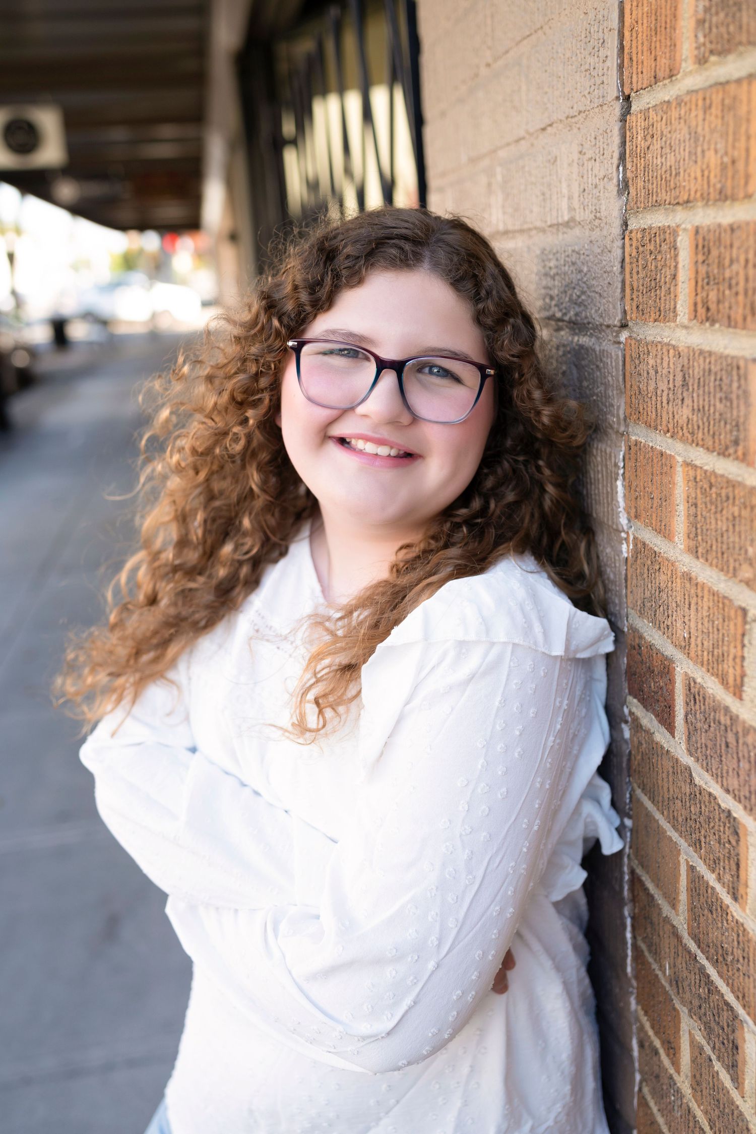 A series of four photos showing someone with curly hair and glasses wearing a white sweater posing against a brick wall.