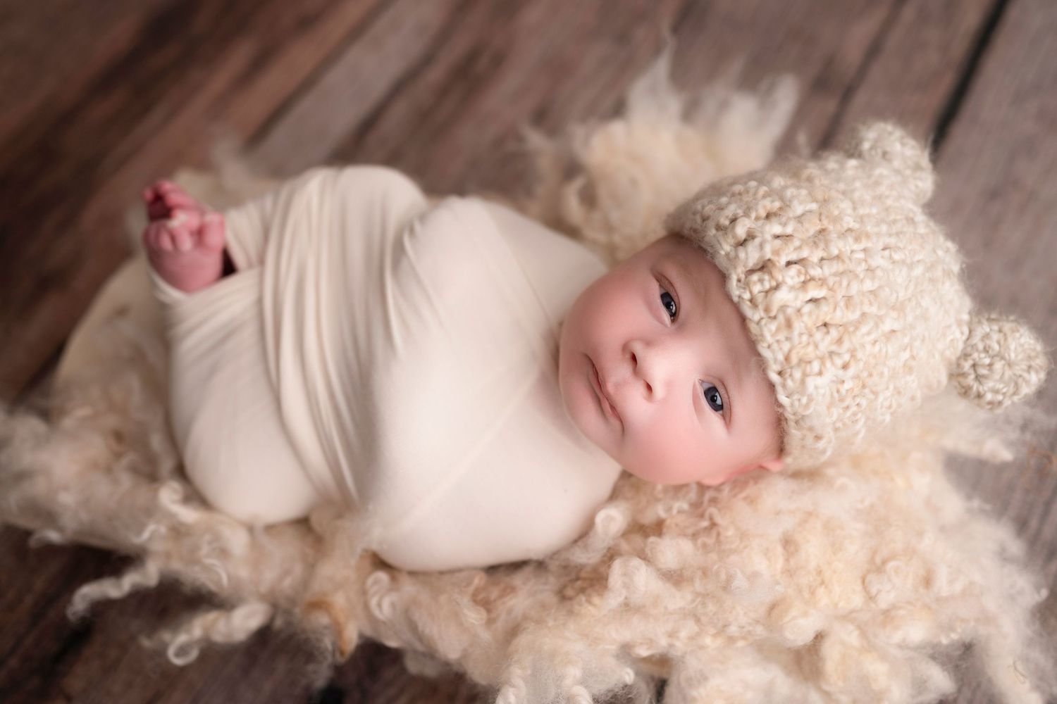 A baby in white lace dress lies on soft white blankets in a series of gentle poses during a professional photo session.
