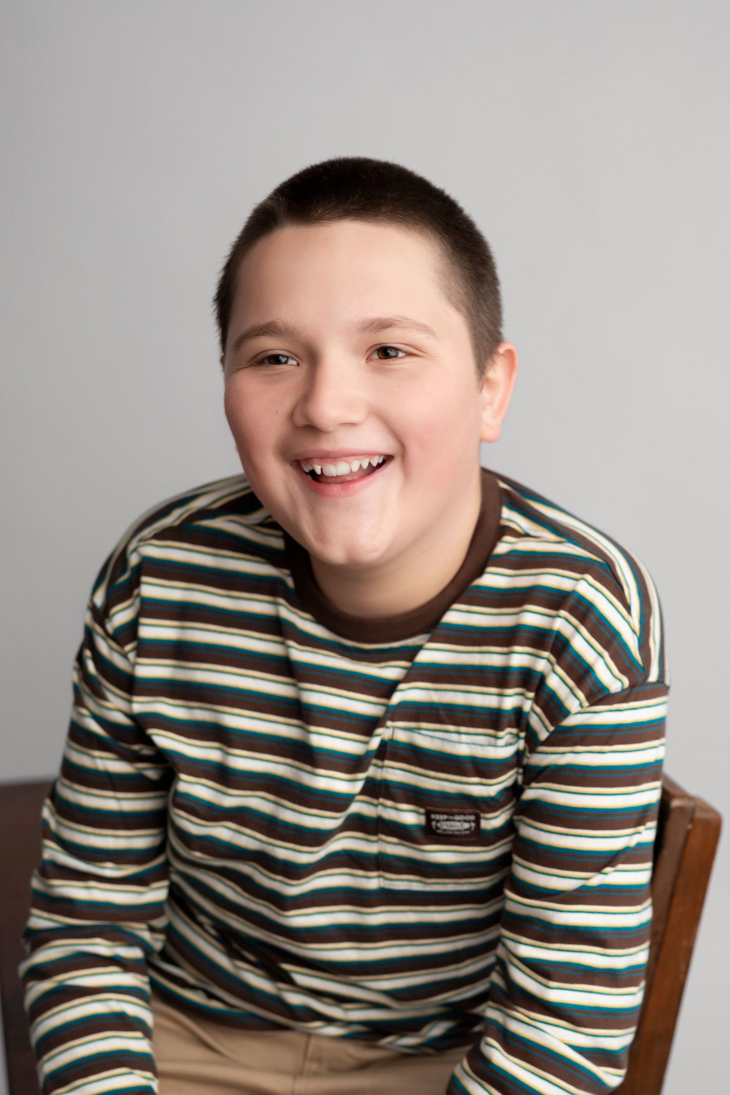 A young person wearing a striped long sleeve shirt smiles warmly at the camera during a portrait session.