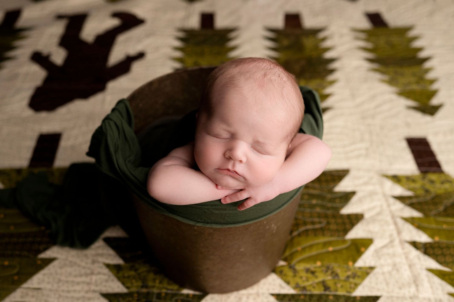 A sleeping newborn baby nestled in a brown basket with green leaf decorations and shadows in the background.