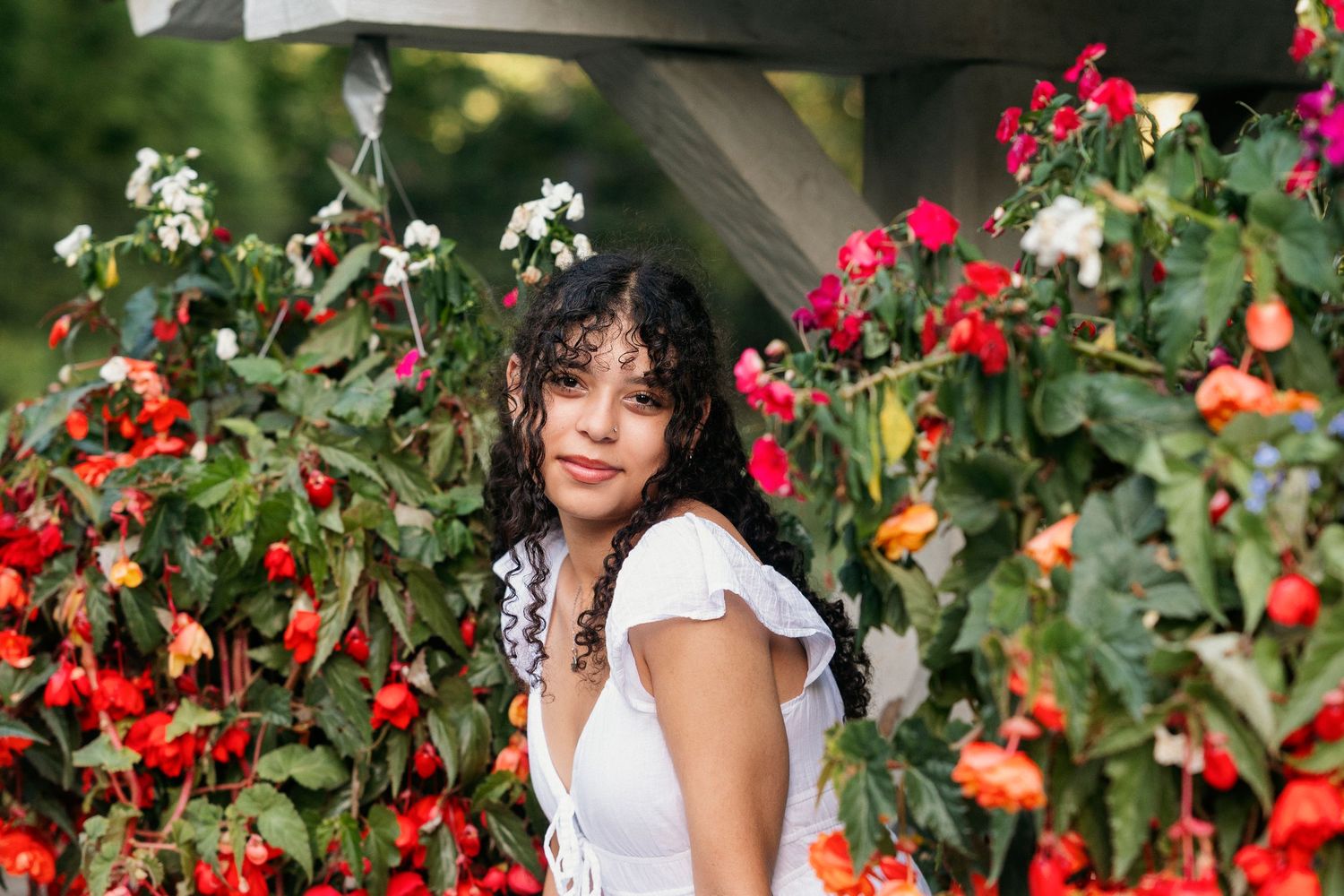 A person poses among vibrant red berries and green foliage in a sunny garden setting.