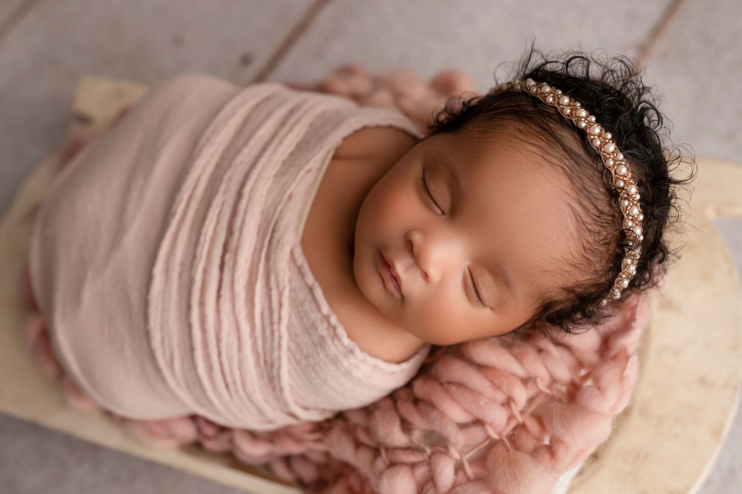 A sleeping newborn baby wrapped in soft pink fabric with delicate lace headband rests peacefully in various poses.