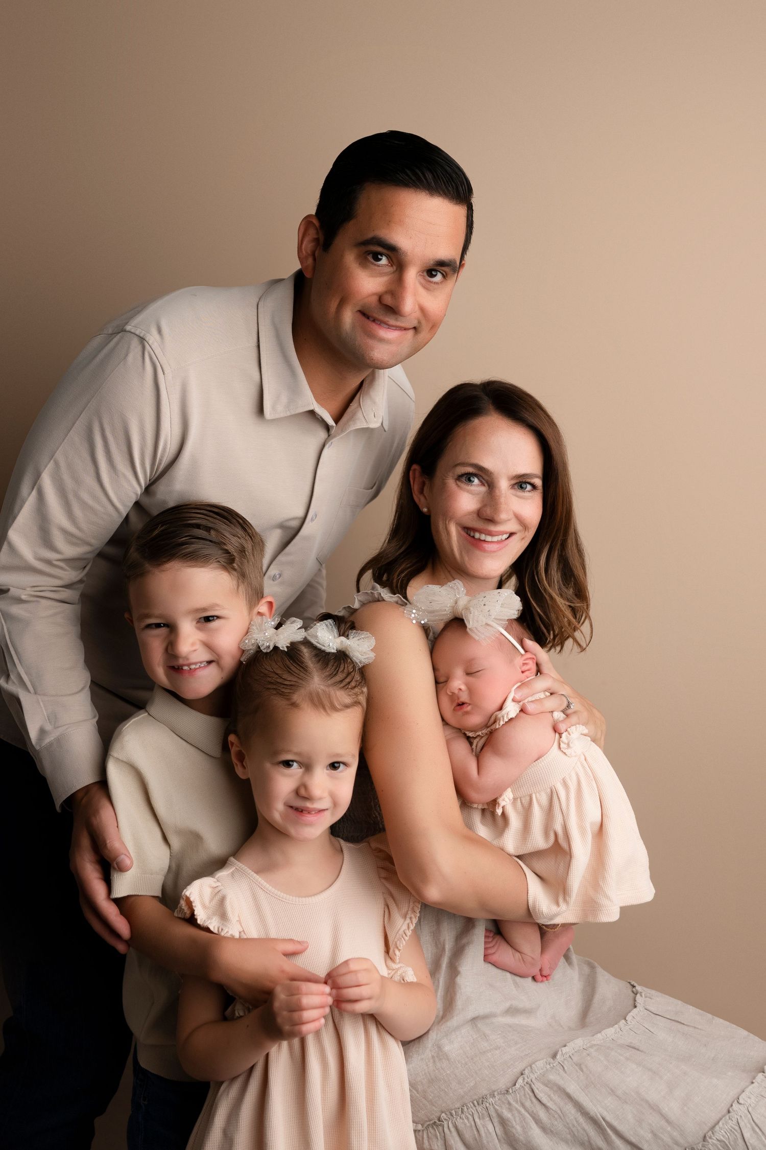 Family portrait series in neutral tones showing parents with two young children and a white cat on beige backdrop.