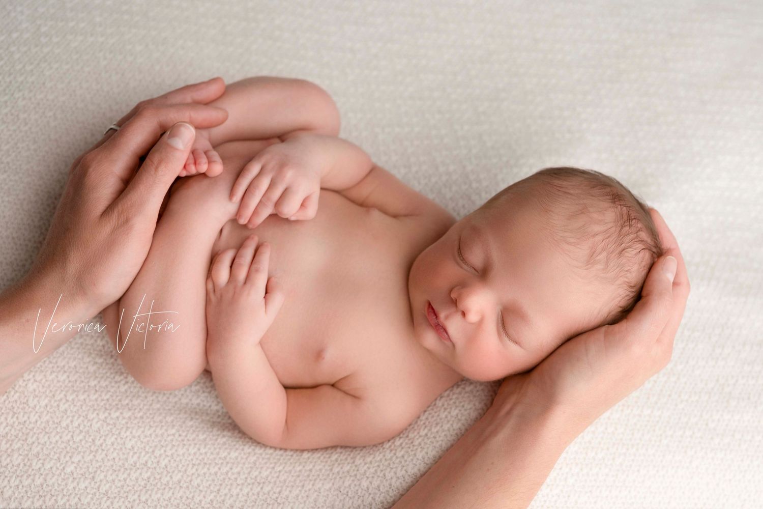 Sleeping newborn curled up on soft white blanket during professional photo session.