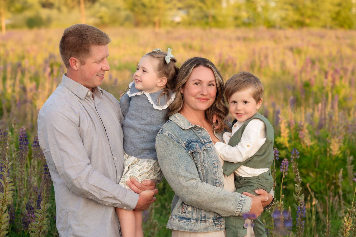 Family in casual attire sharing tender moments together in golden wildflower field during sunset photoshoot.