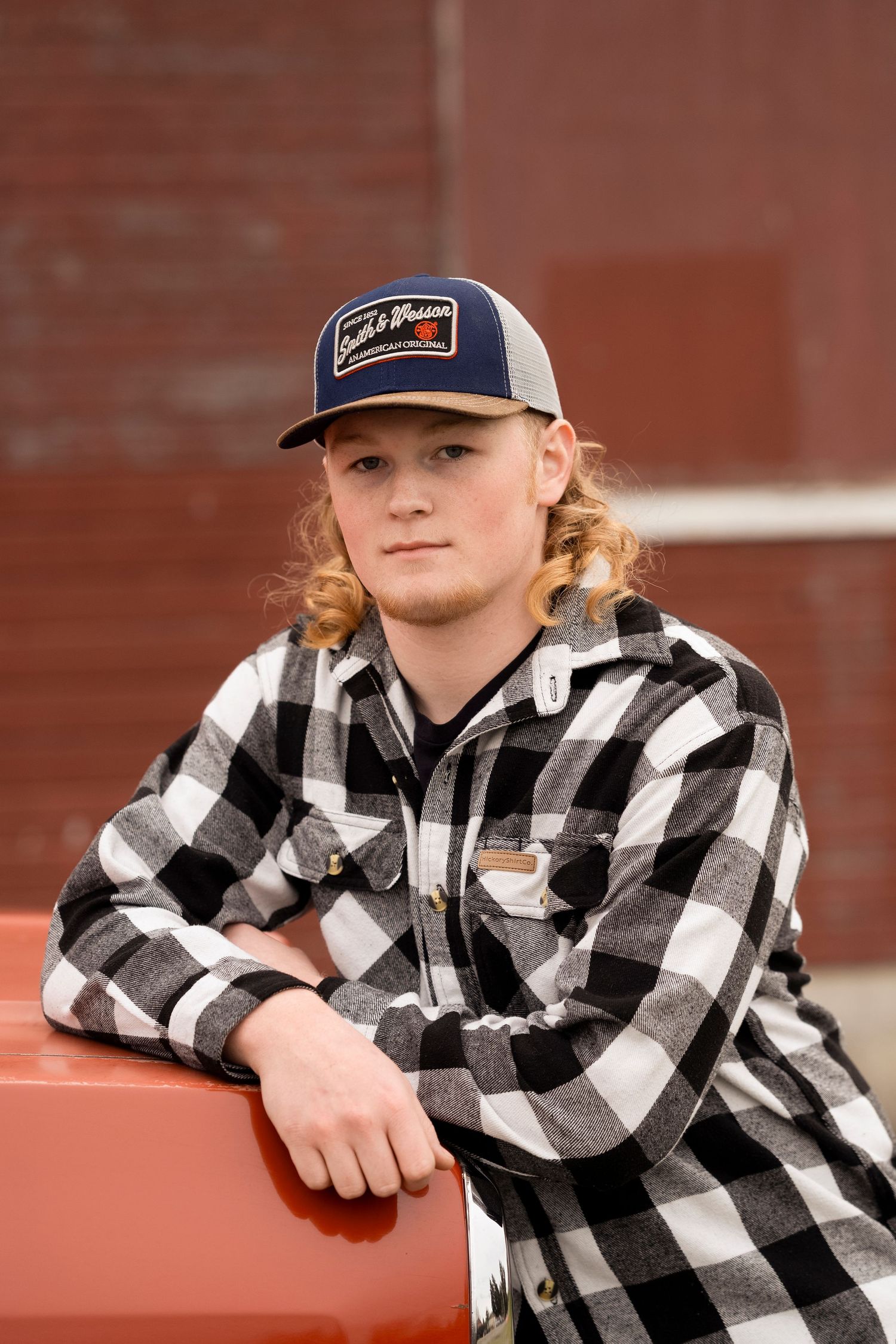 A person in a black and white buffalo plaid shirt and baseball cap leans on a reddish surface in a photo series.