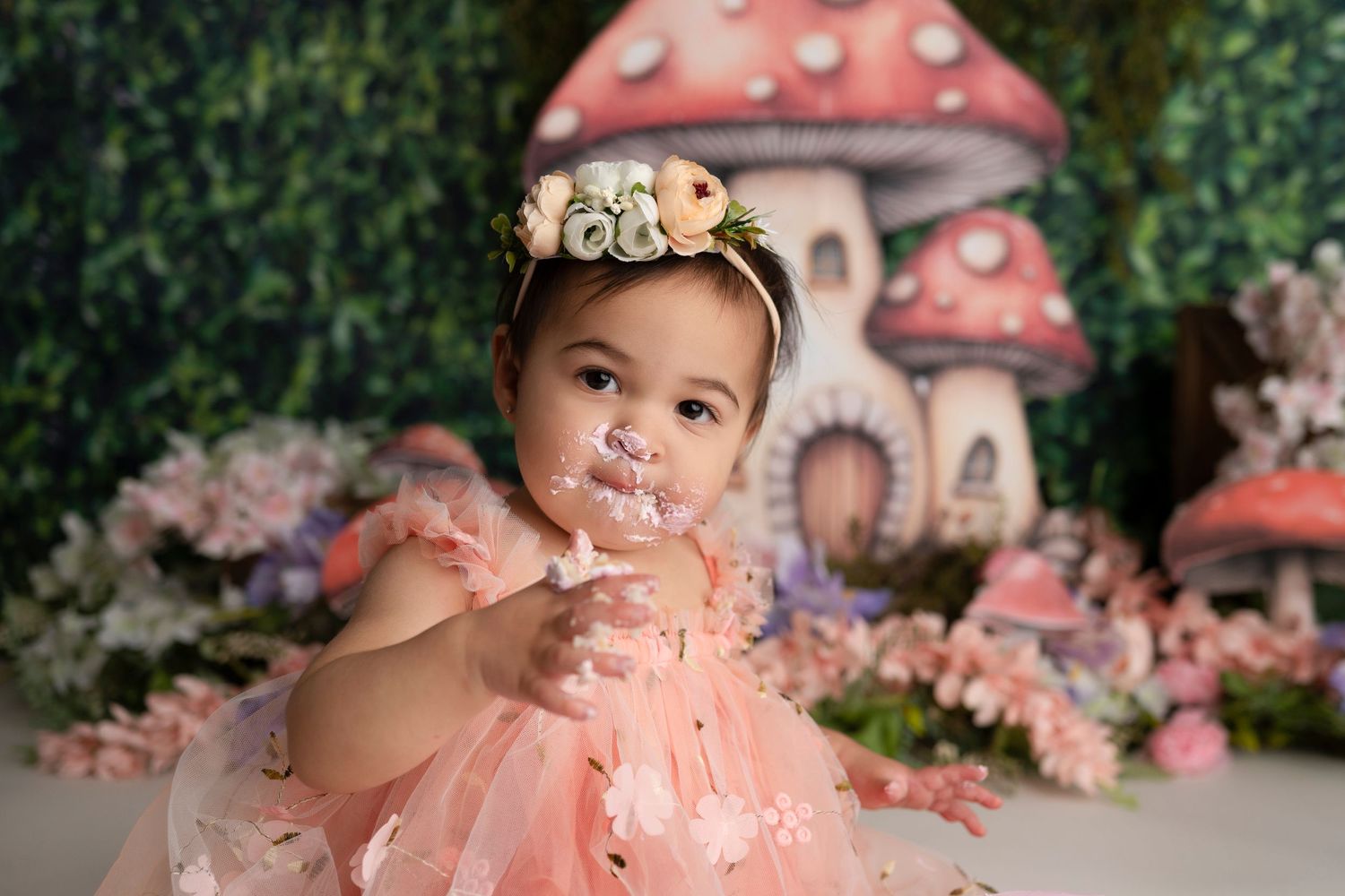 A whimsical pink and white mushroom-themed photo setup with floral decorations creates a magical woodland scene.