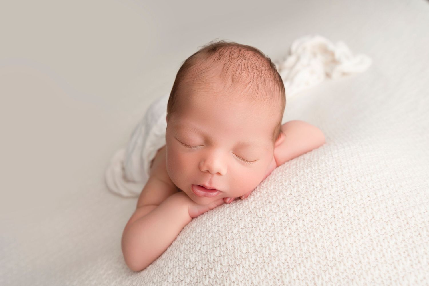 Sleeping newborn baby wrapped in white blanket on soft textured background.