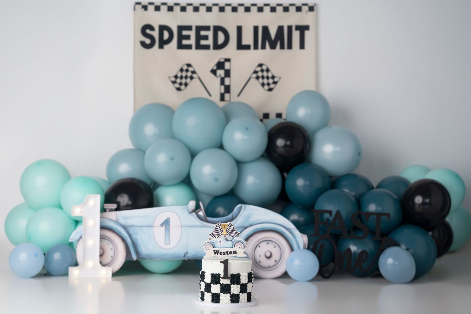 A race car themed first birthday setup with blue balloons, a toy car, and a Speed Limit sign backdrop.