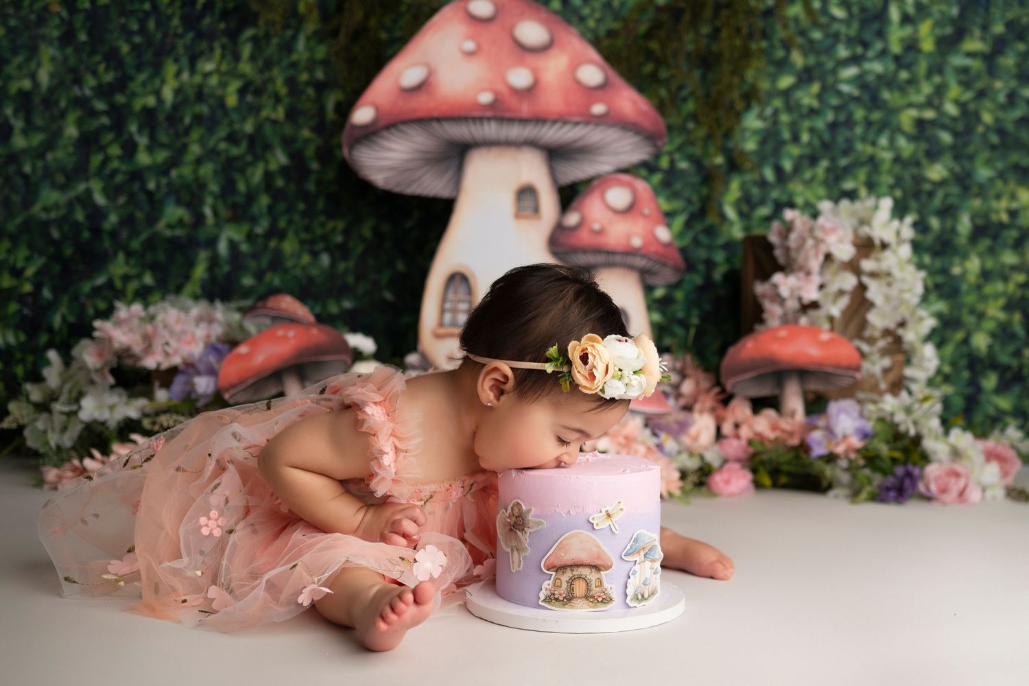 Enchanted woodland cake smash scene with pink mushroom house decorations and floral accents.