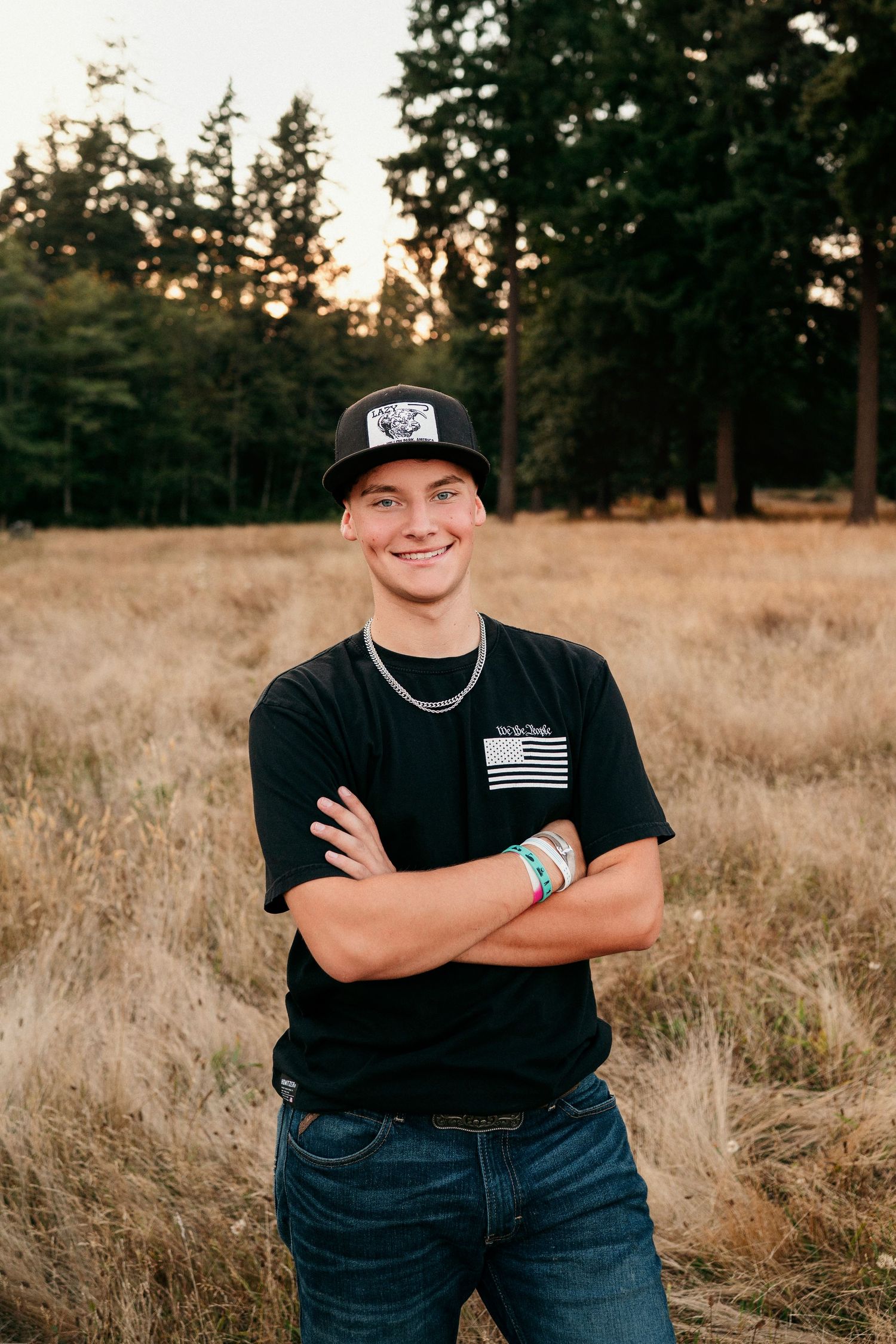 A person in a black t-shirt with a flag patch stands in a golden field at sunset.
