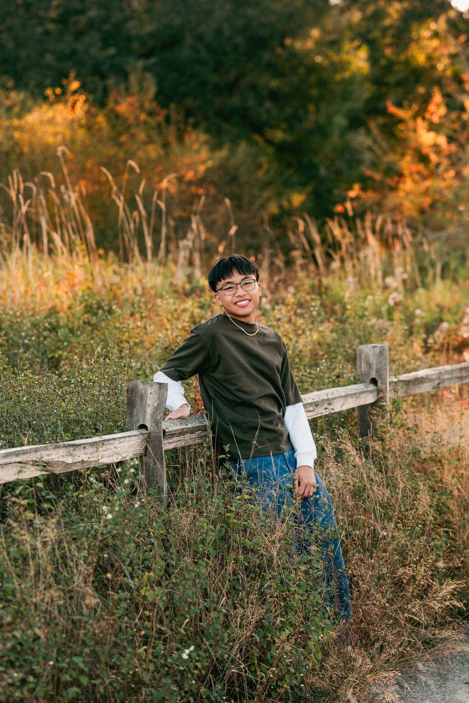 A child in a green sweater and jeans plays near a rustic wooden fence during golden hour in a wildflower meadow.