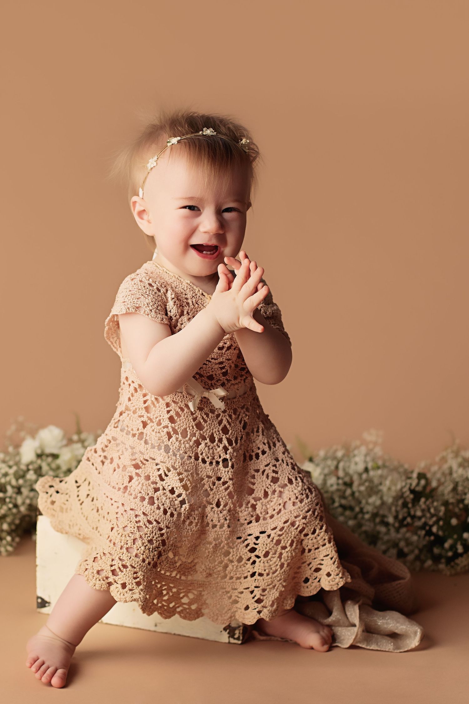 A series of photos showing a giggling baby wearing a delicate cream lace dress against a neutral beige background.