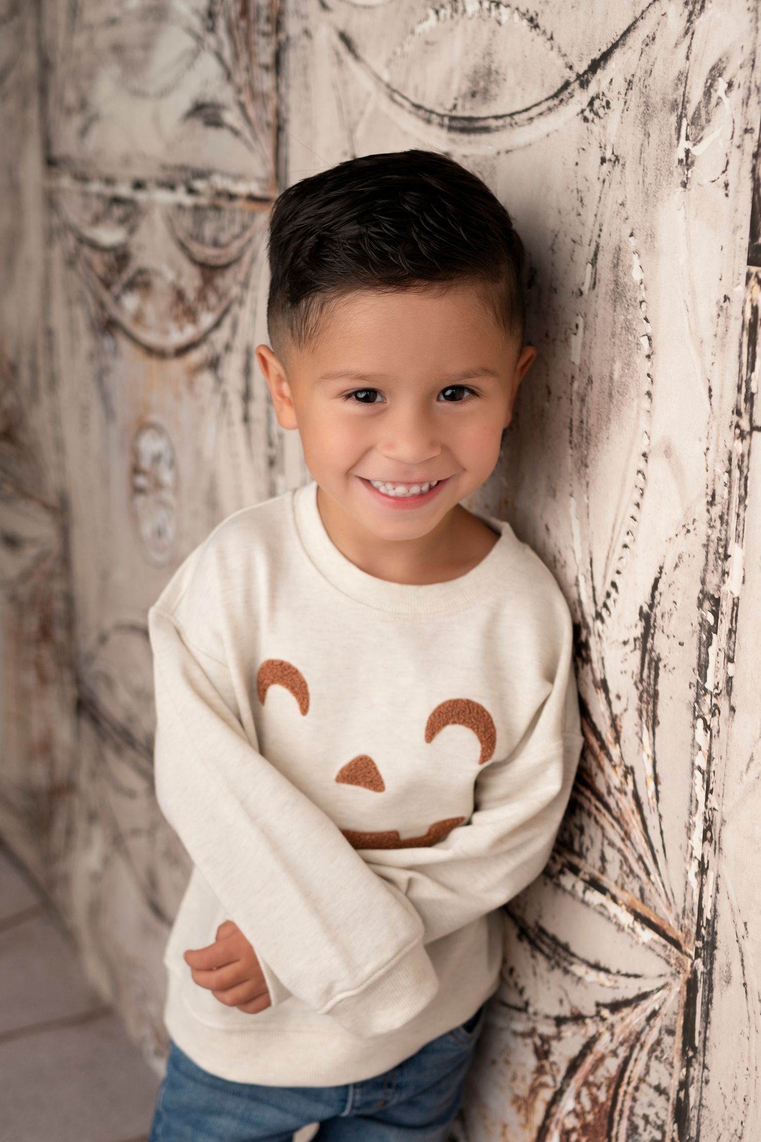 A series of candid portrait shots showing a child wearing a cream sweater and jeans against a white textured background.