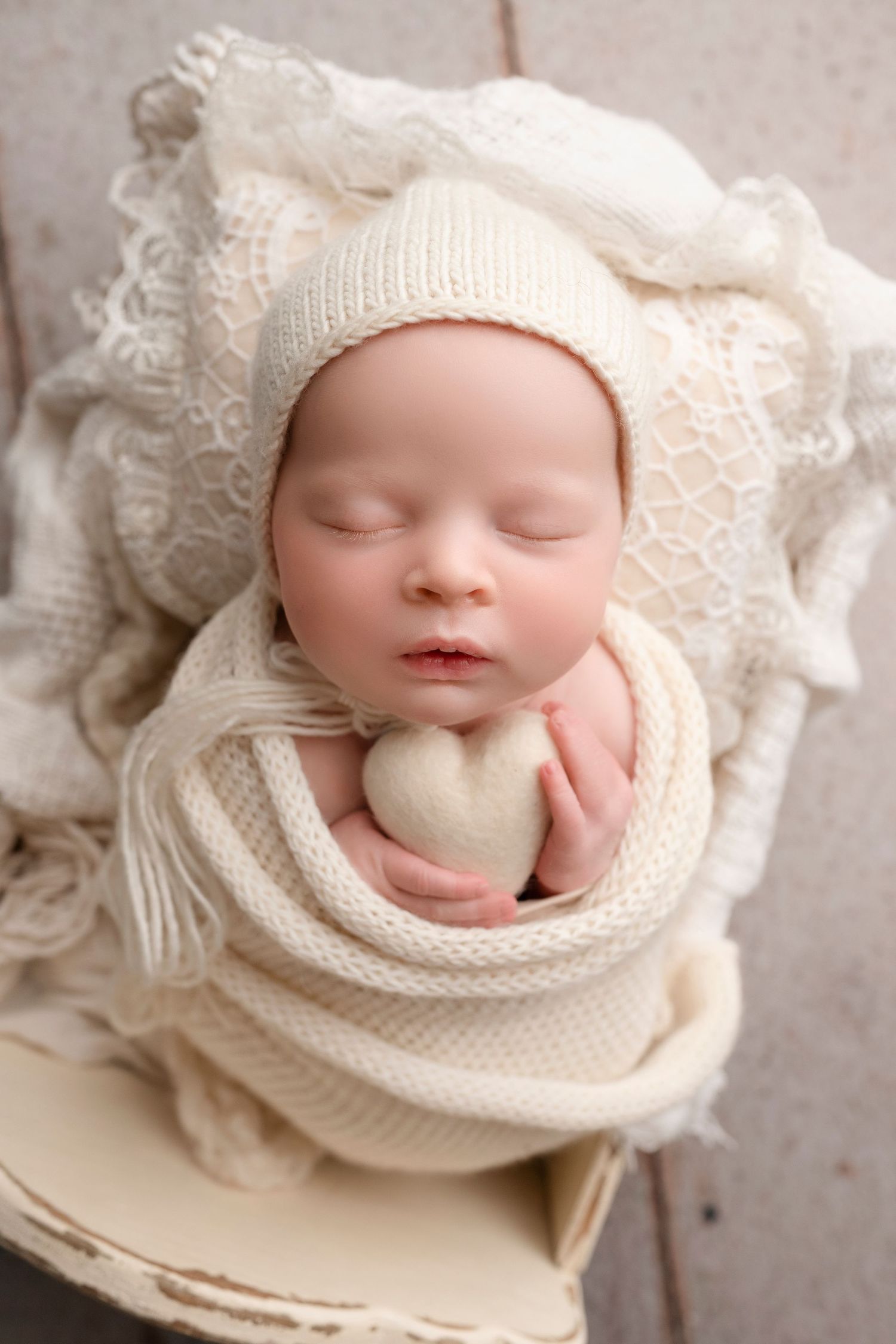 Artistic newborn portrait with baby wrapped in soft cream knit blankets and lace against neutral background.