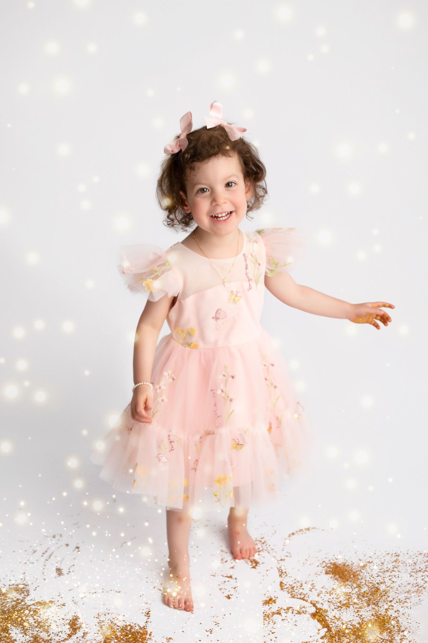 A playful child in a peach-colored dress dances among scattered gold glitter on a white floor.