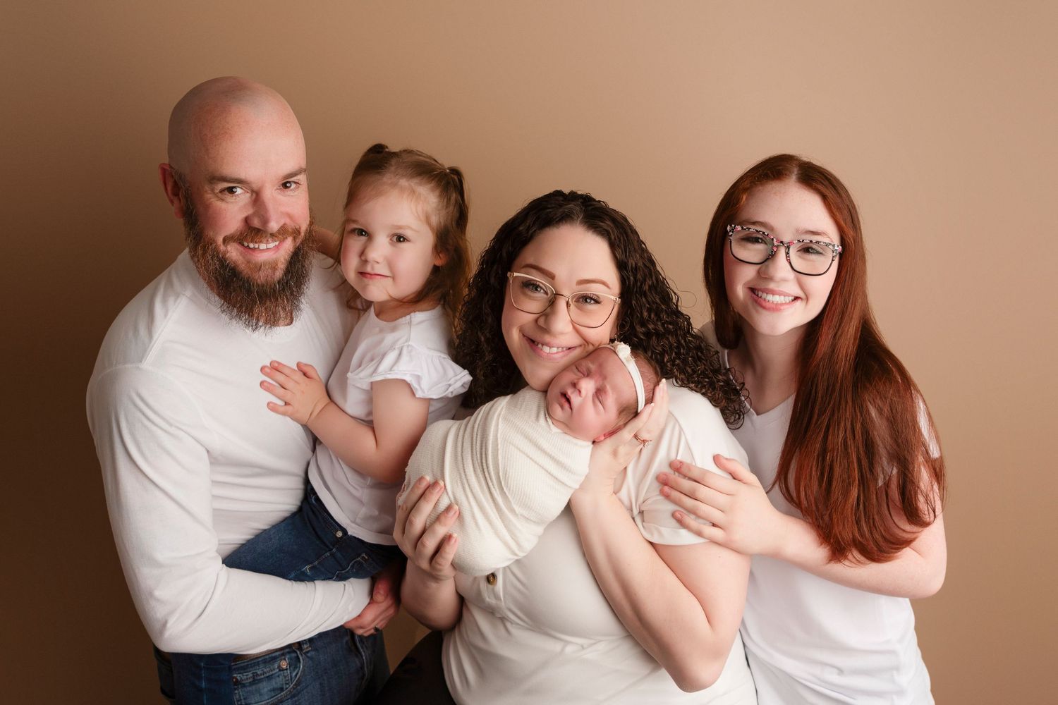 A family wearing white and cream colored clothing poses together for a series of warm, intimate portrait photographs.