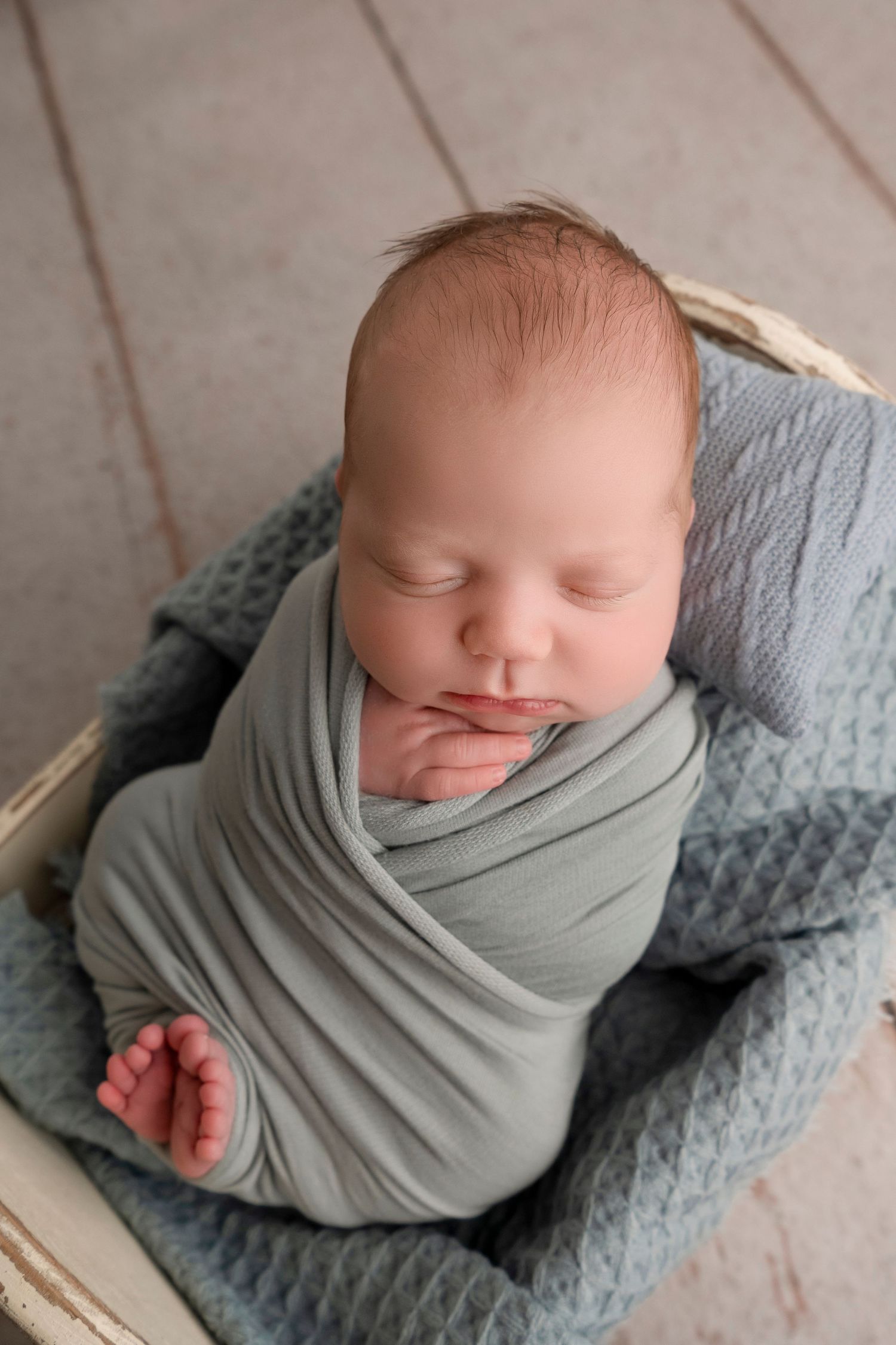 A sleeping newborn baby wrapped in a soft gray swaddle blanket lies on a textured blue blanket.