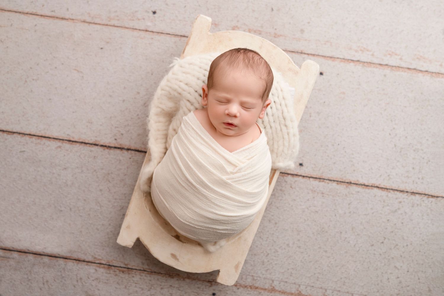 Newborn photography series showing baby wrapped in cream fabric against white wooden backdrop.