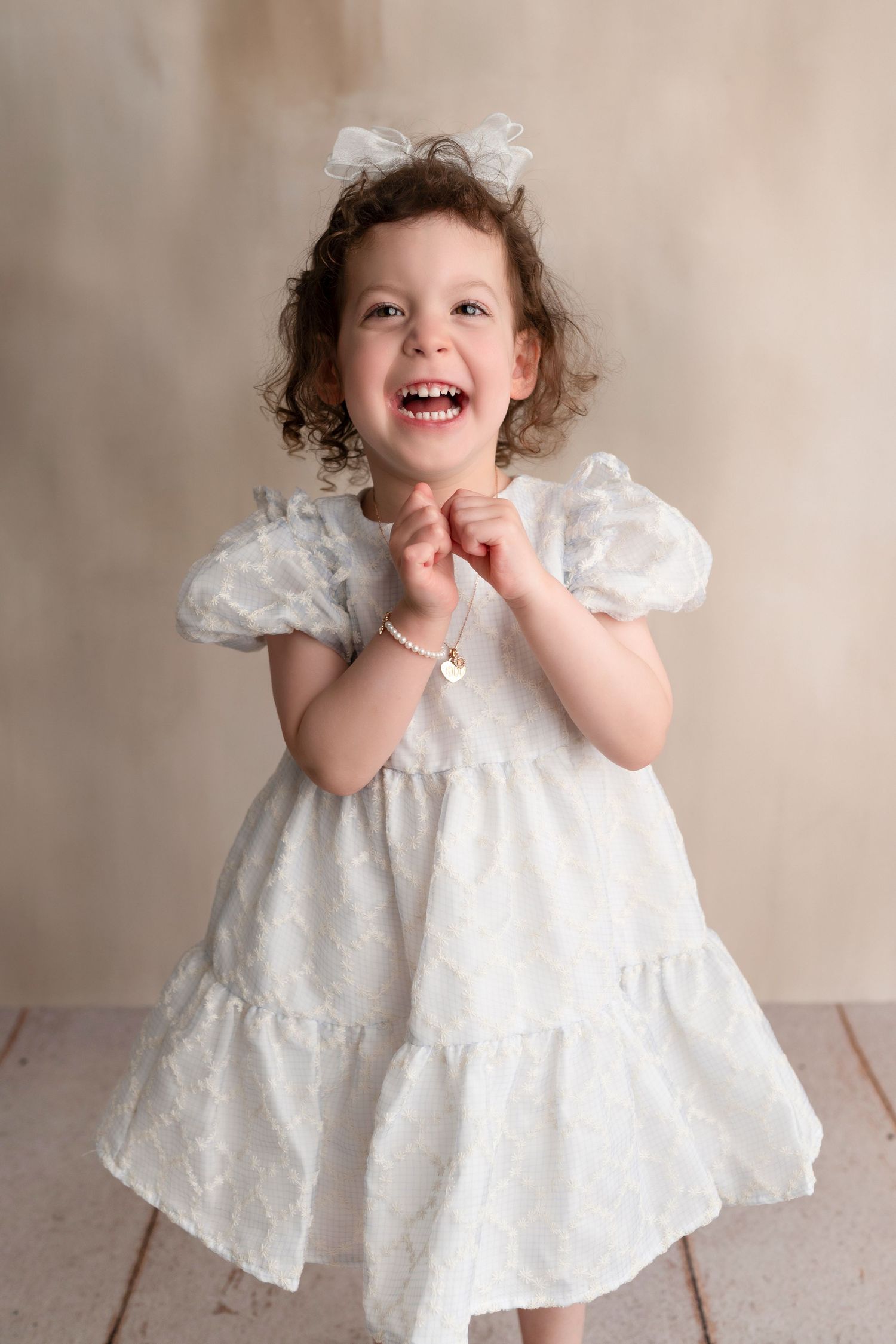 A series of photos showing a small child in a white lace dress twirling and expressing joy against a neutral background.