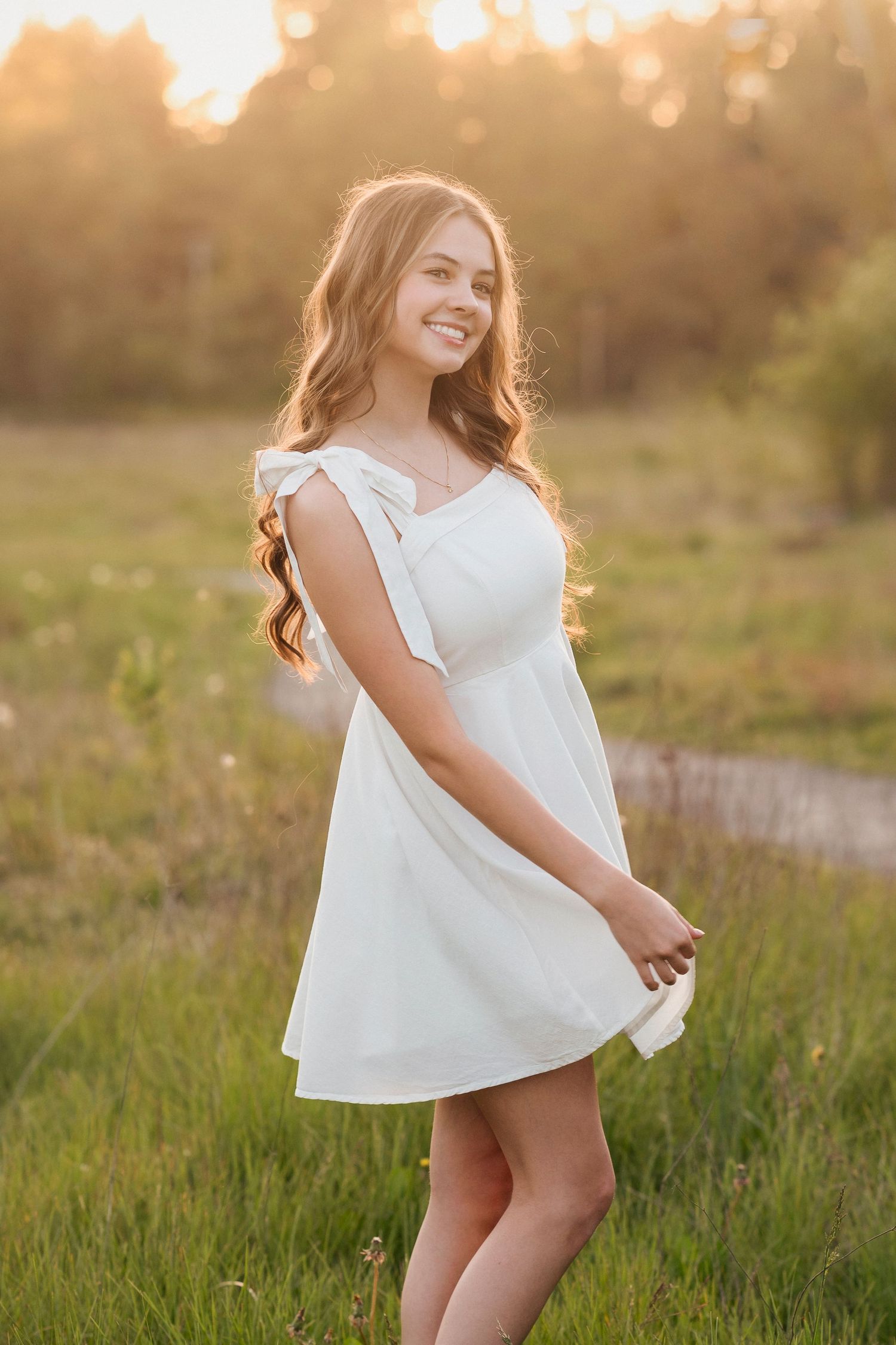 A young girl in a white dress twirls playfully in a sunlit meadow during golden hour.