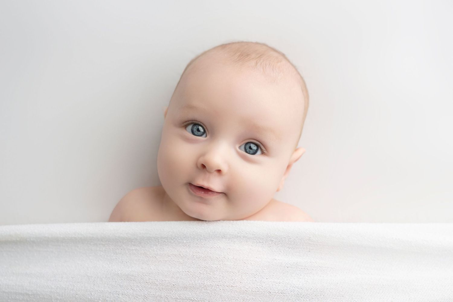 Close-up portrait of baby with bright blue eyes against white background.