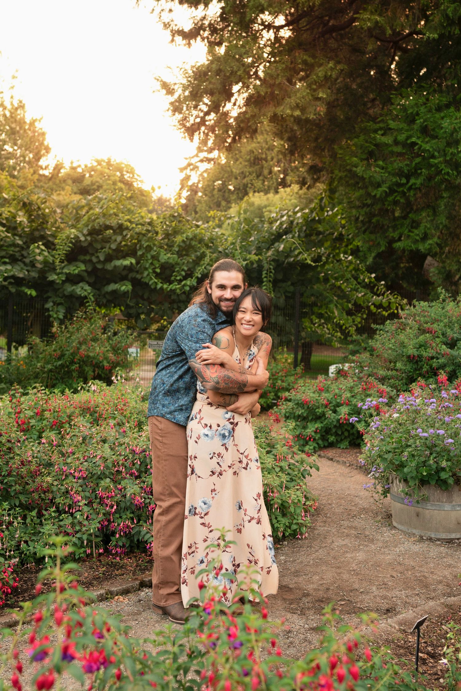 A couple embraces in a beautiful garden at sunset surrounded by blooming flowers and winding paths.