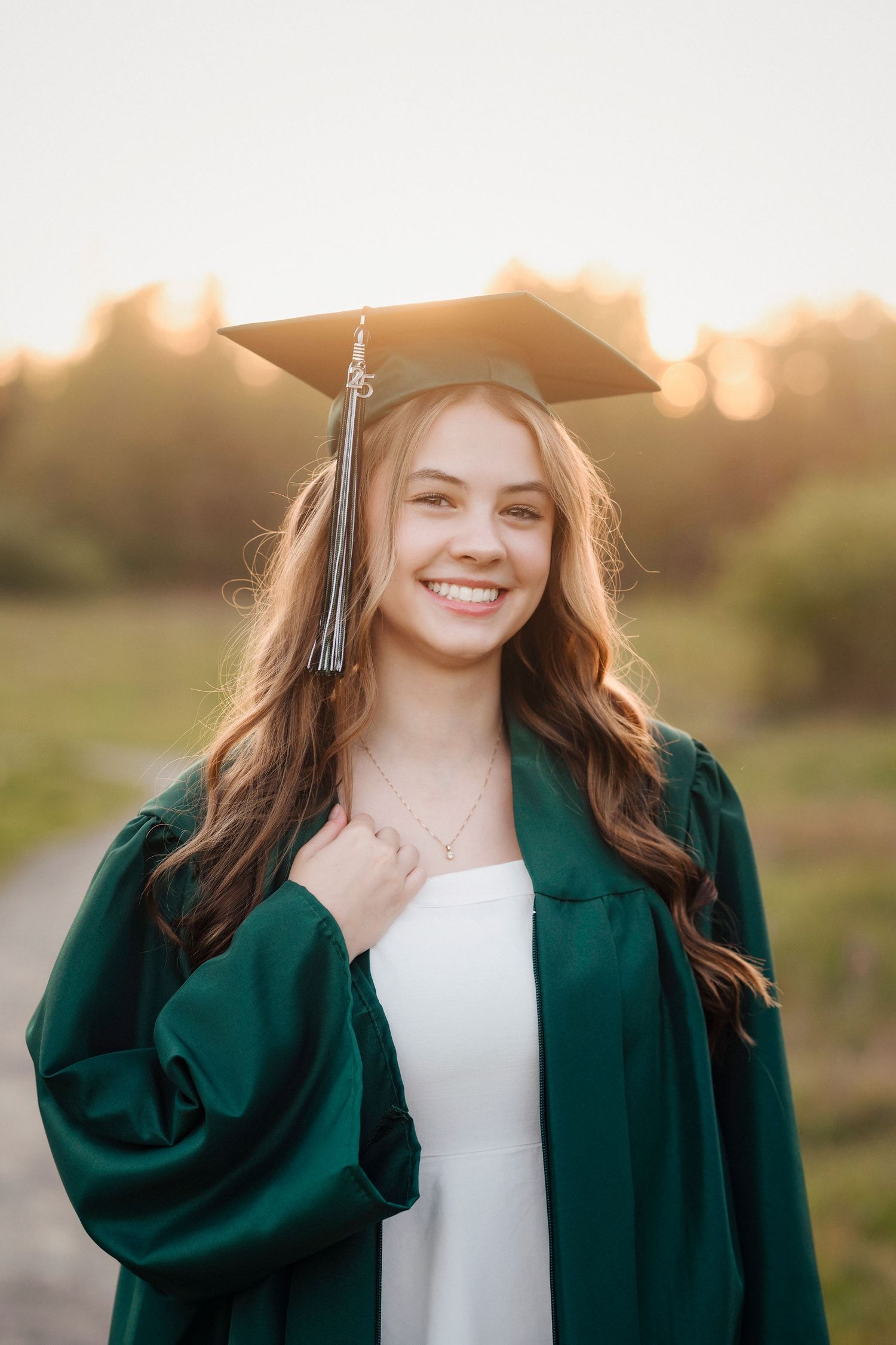 Graduate in emerald green cap and gown smiles during outdoor sunset photo session.