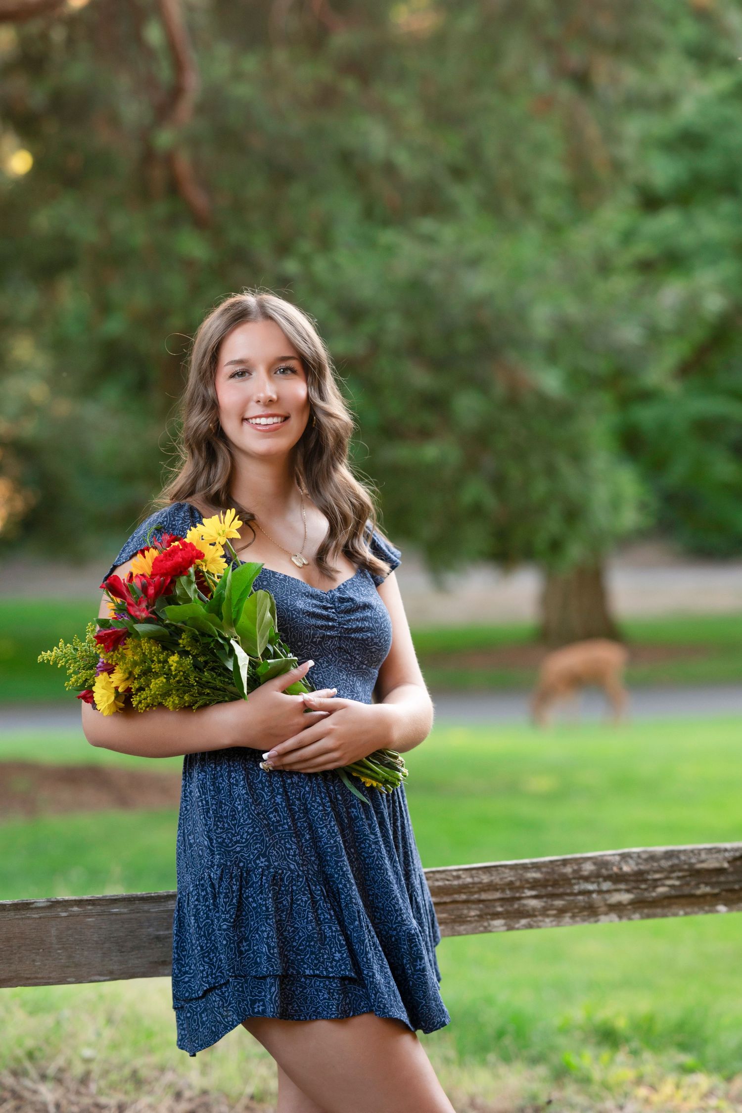 A person in a navy blue dress holds a colorful bouquet of flowers while standing outdoors in a park setting.