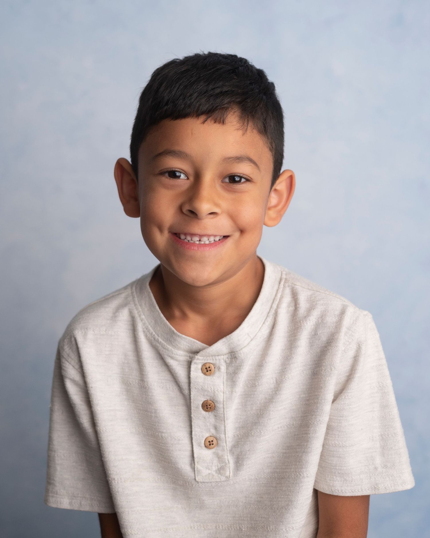 Young student wearing a light colored henley shirt poses for a school portrait against a blue backdrop.
