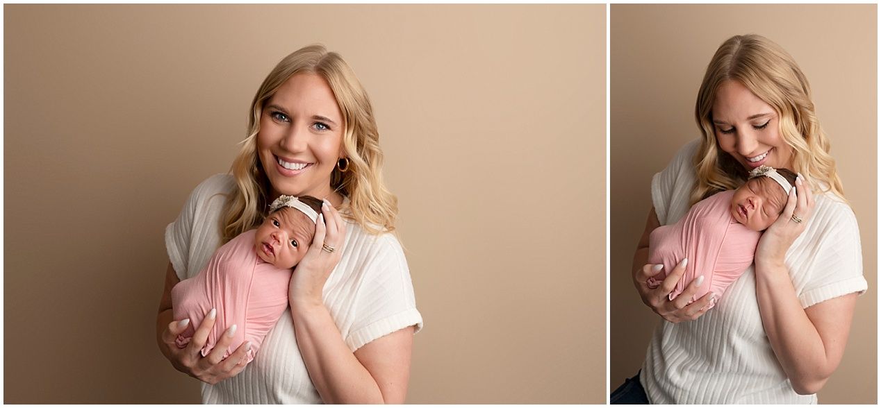 Smiling blonde mother in white top holds sleeping newborn wrapped in pink in a professional studio portrait.