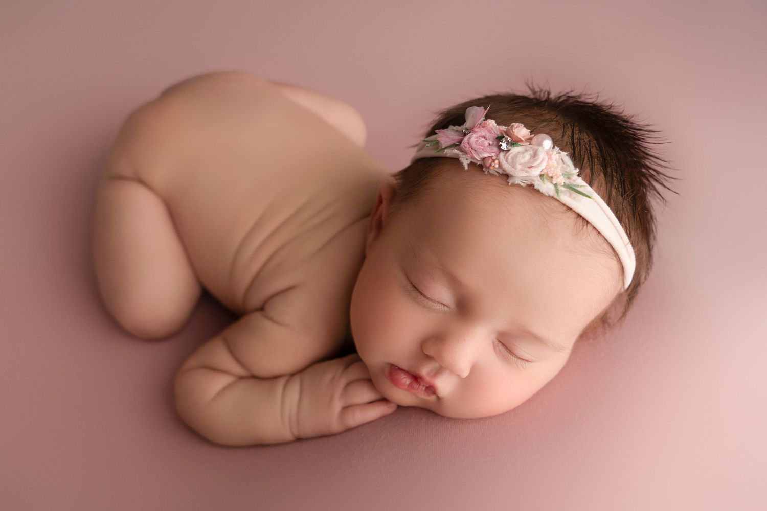 Sleeping newborn wrapped in soft pink fabric against pink backdrop.