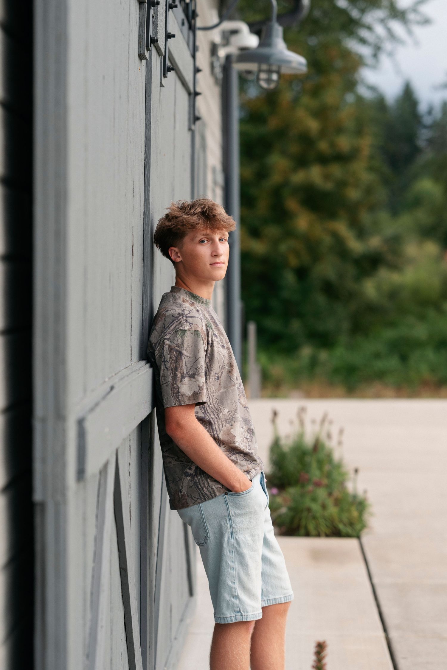 A person leans against a white wall wearing casual summer attire in an outdoor setting.