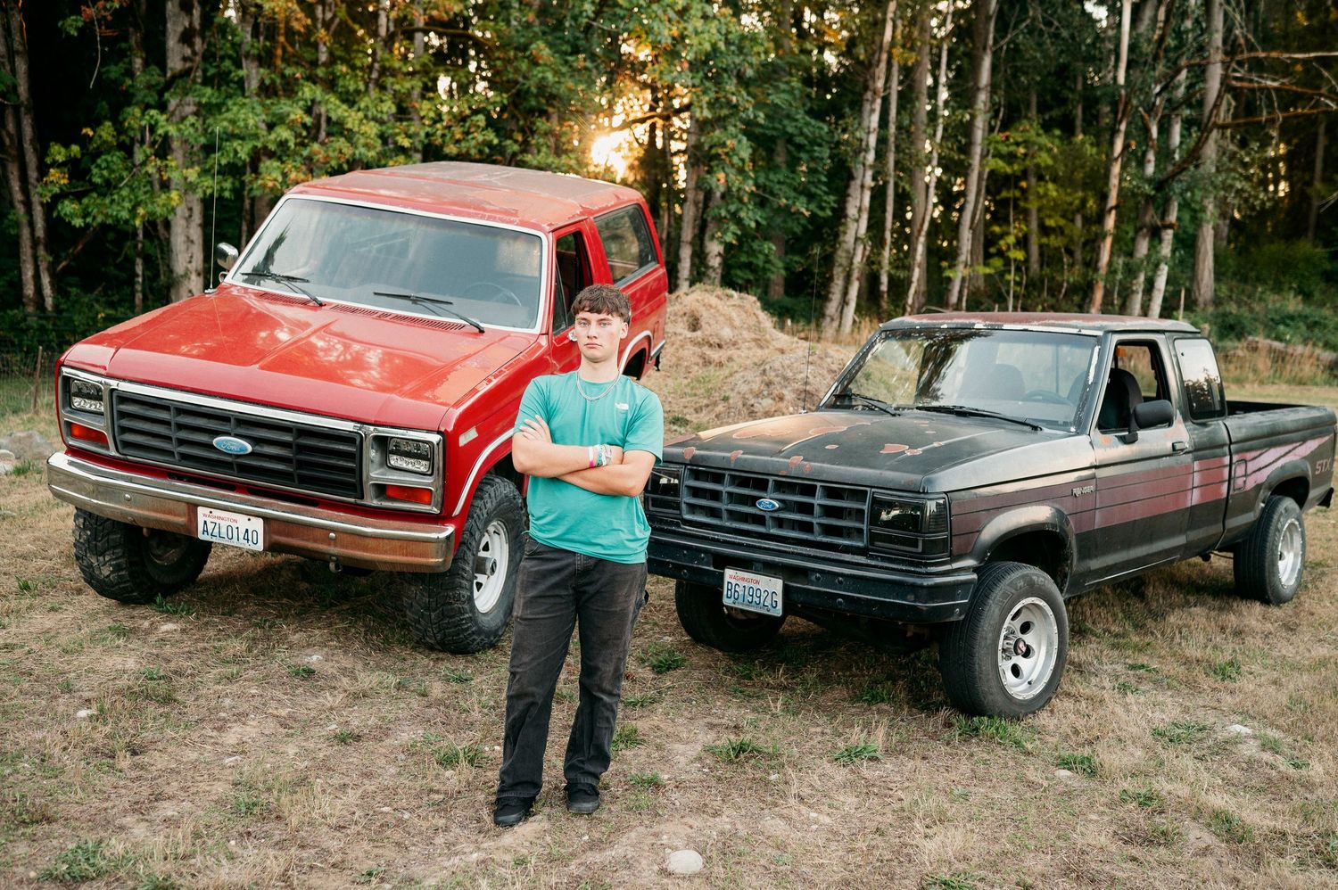 A series of vintage red and black pickup trucks parked on a wooded hillside with someone standing nearby.
