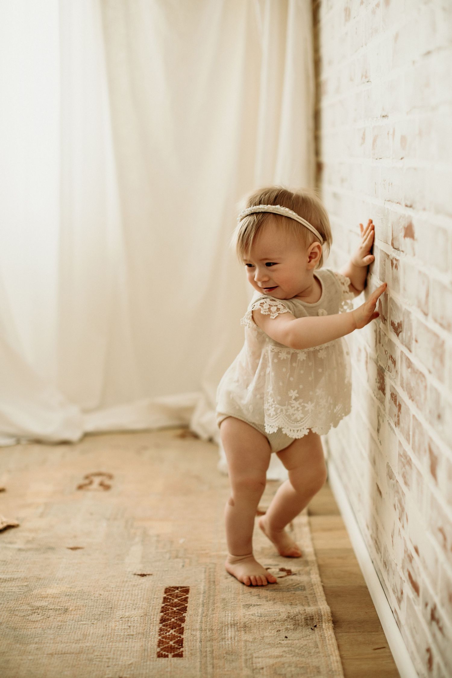 A series of connected images showing a baby crawling along a white brick wall wearing a delicate lace romper.