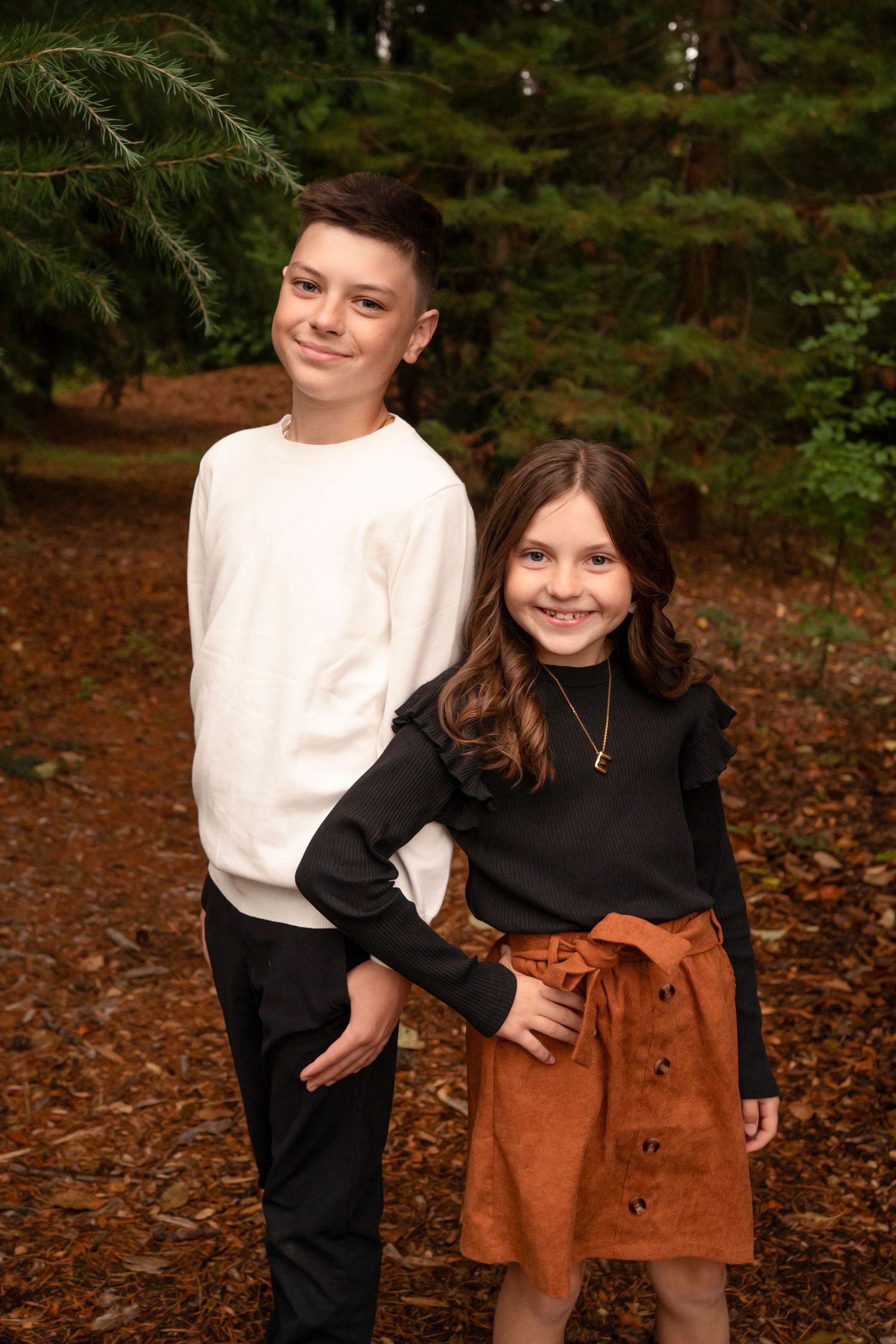 Two children in contrasting black and white outfits pose playfully in autumn leaves.