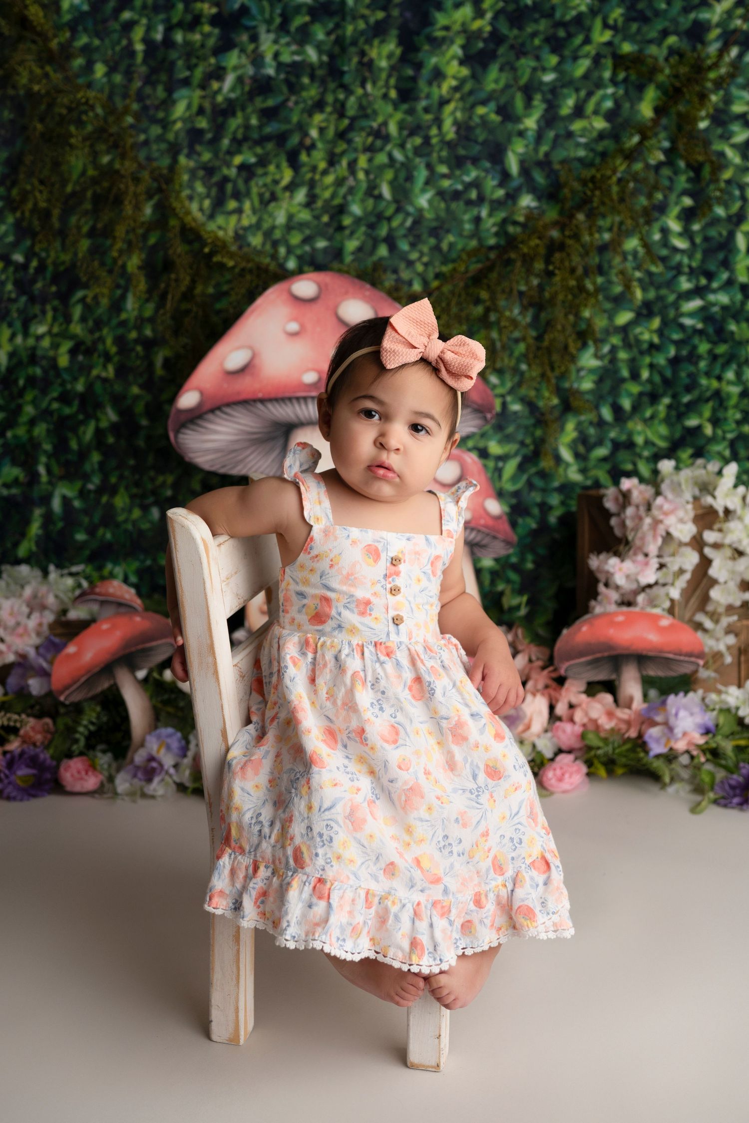 Sweet nursery photo setup with floral dress, pink mushroom props, and leafy green backdrop.