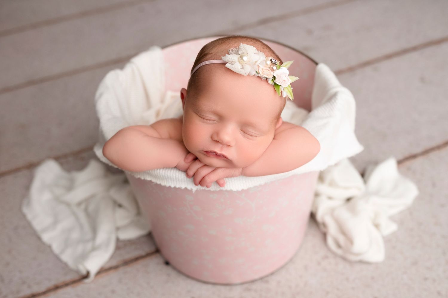 Newborn baby sleeping peacefully in a soft pink bowl surrounded by white fabric.