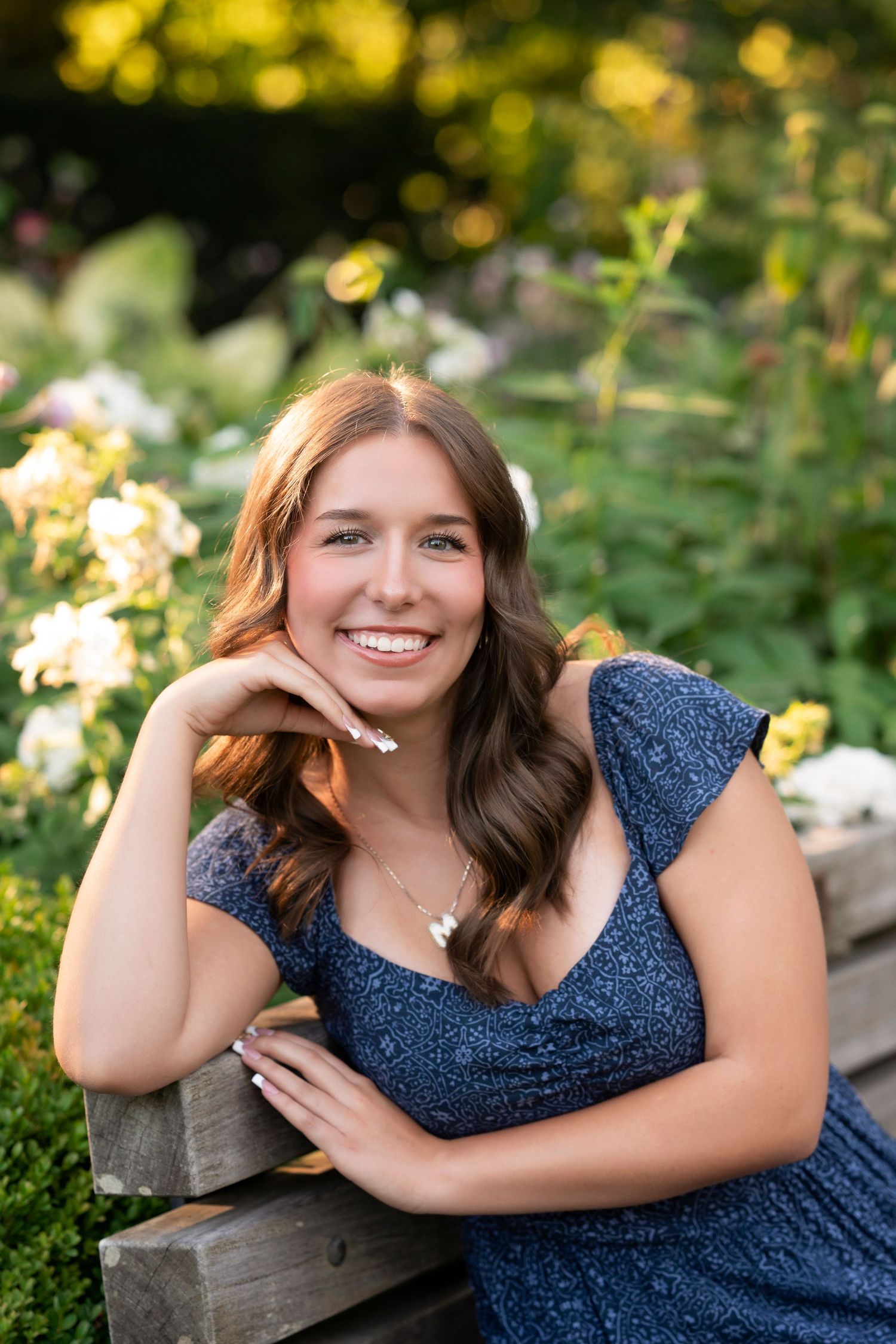 A person in a sparkly navy blue dress poses outdoors against natural greenery and sunlit background.